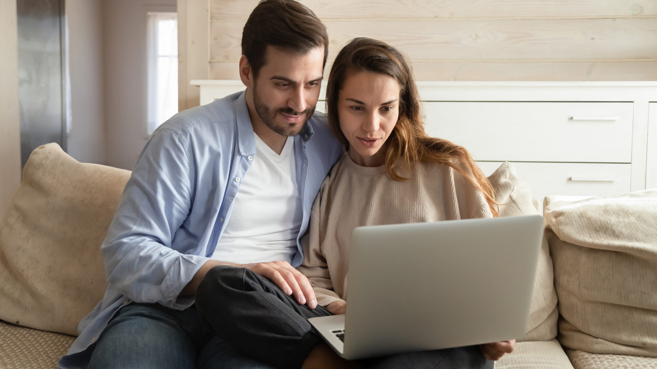 Couple looking at a laptop on the couch while planning their wedding music